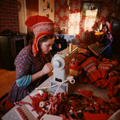 Saami woman sews yards of ribbon and trim onto her wedding dress. Kautokeino. Norway. 1972