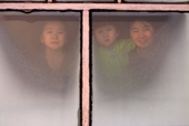 Lena Potapova & her sisters Varya & Tanya look through a window at their home in Verkhoyansk, Yakutia Siberia. 1999
