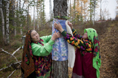 Irina Purgurchina (left) & her friend Vera, Khanty women, tie material round a sacred tree that protects her youngest son. The material sybolises her son's clothing. Yamal, Western Siberia, Russia.